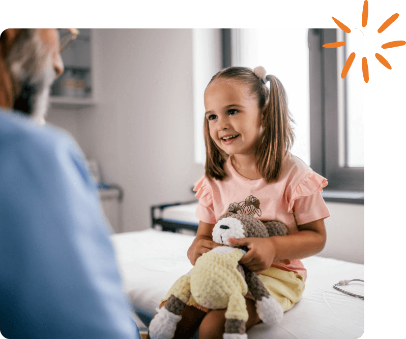 Smiling child holding a stuffed animal during a pediatric visit.