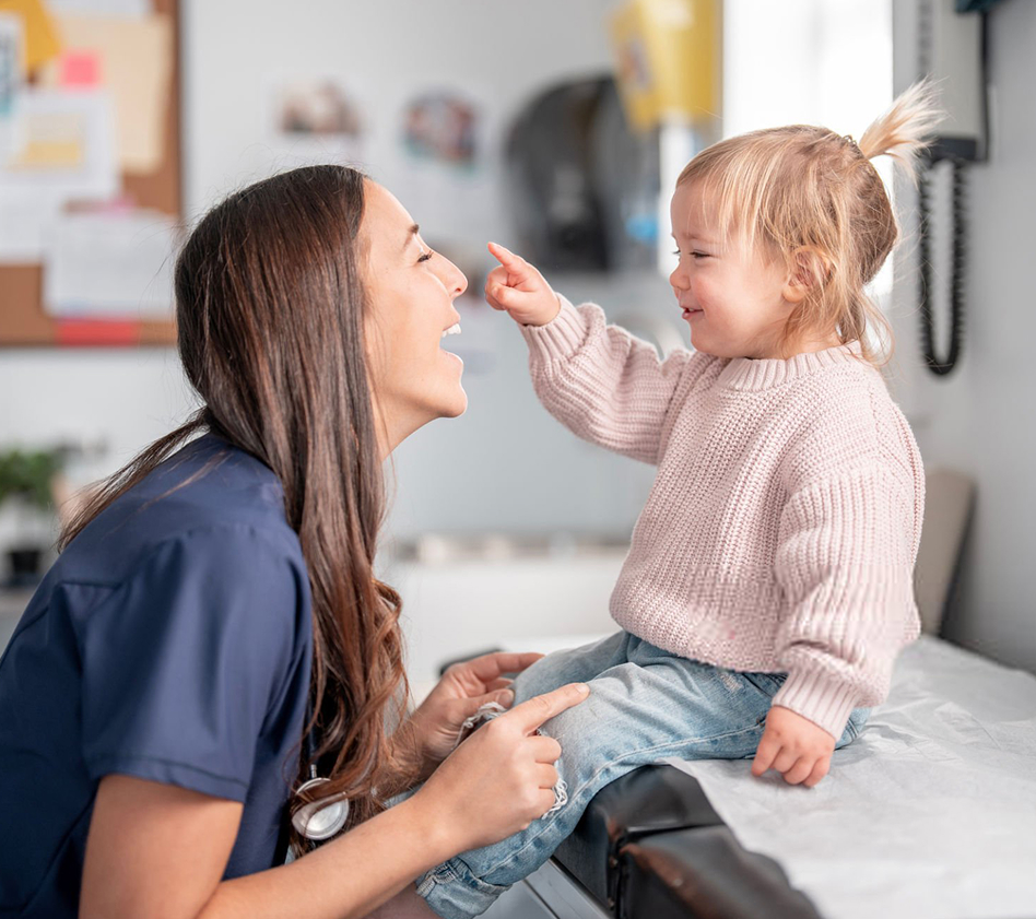 Toddler smiling and pointing at a healthcare provider during a playful checkup.