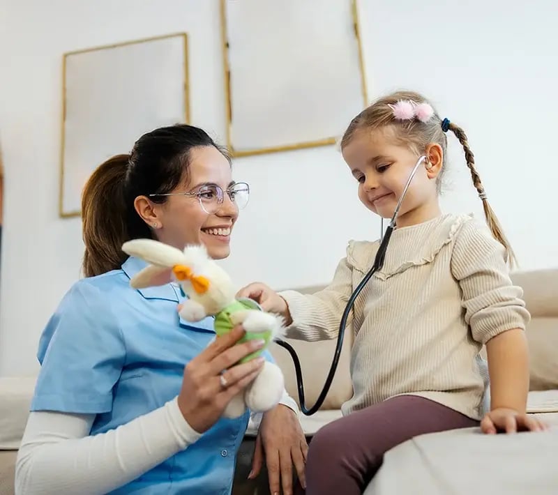Child listening to a stethoscope while smiling with a healthcare provider during a playful checkup.